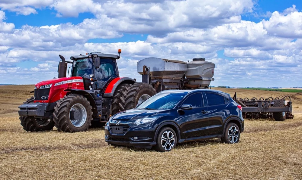 Carro SUV azul-escuro ao lado de um trator vermelho no campo